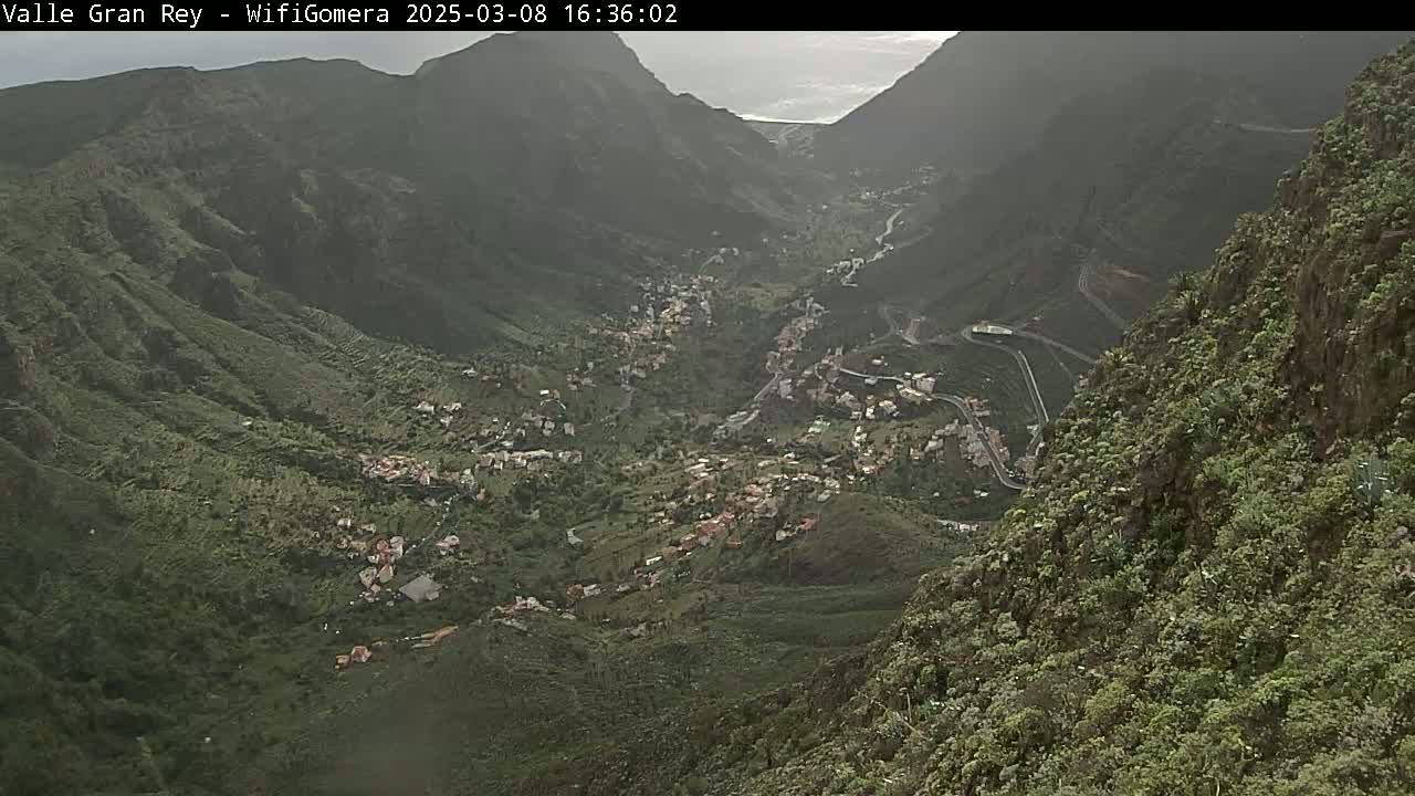 A hazy view shows a valley town nestled between steep, green mountains.