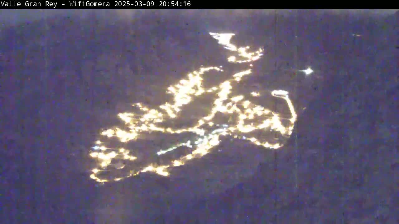A nighttime aerial view shows a town's lights scattered across a dark landscape.