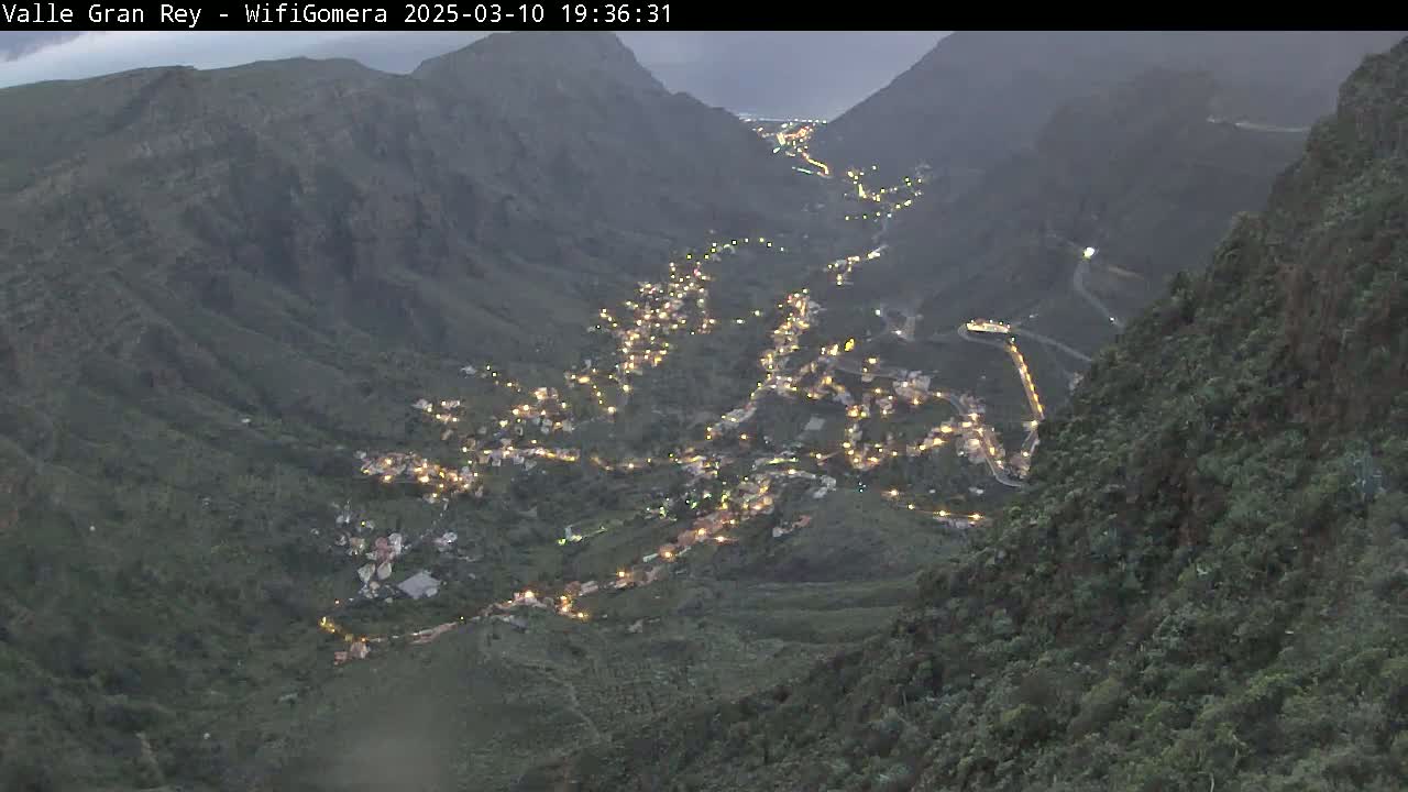 A village nestled in a dimly lit valley between dark, mountainous slopes under a dusky sky.