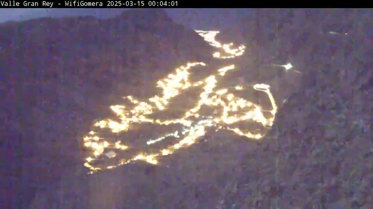 A nighttime aerial view shows a valley with numerous lights illuminating roads and buildings.