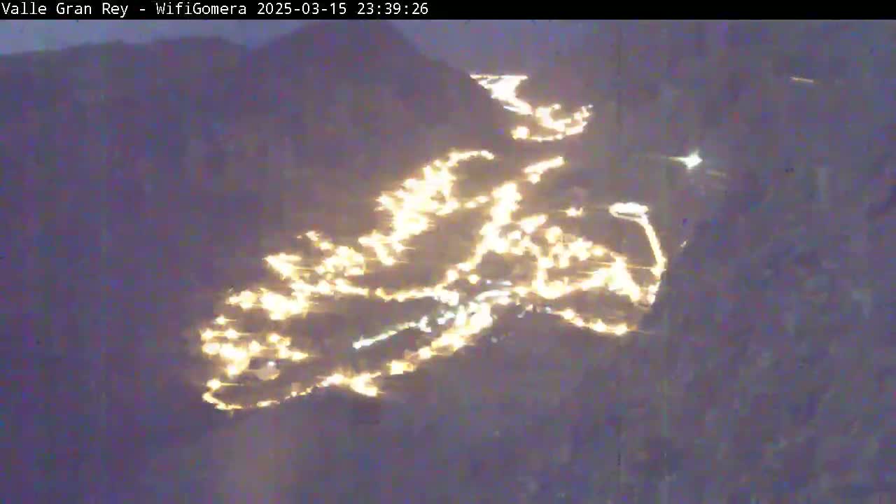 A nighttime, aerial view shows a town nestled in a valley illuminated by numerous lights.