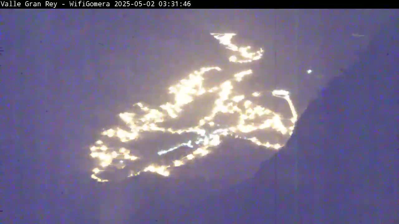 A nighttime view shows city lights reflecting off low-lying clouds.