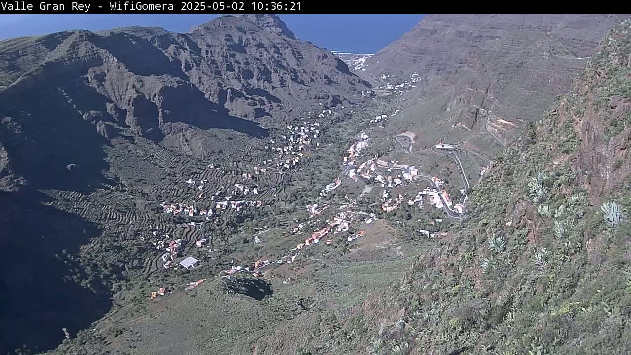A mountain valley town nestled between steep, rocky mountains under a clear, sunny sky.