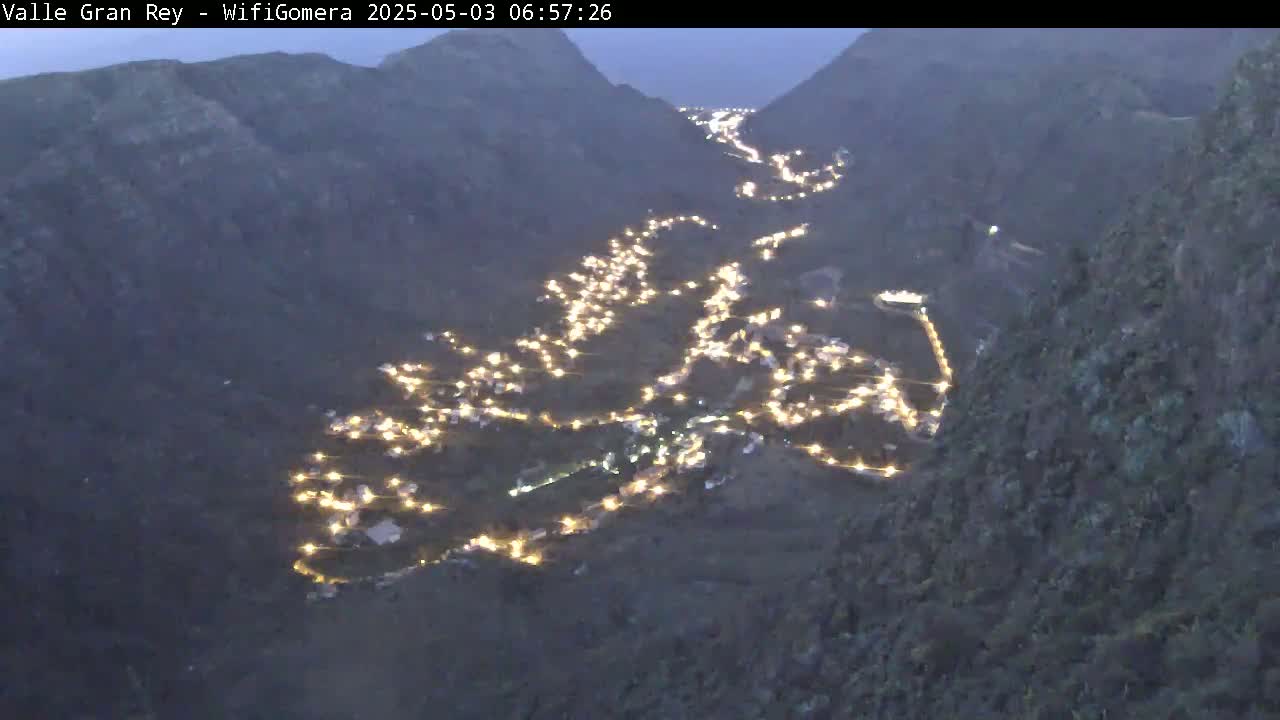 A valley at night is illuminated by the lights of a town nestled within its mountainous terrain.