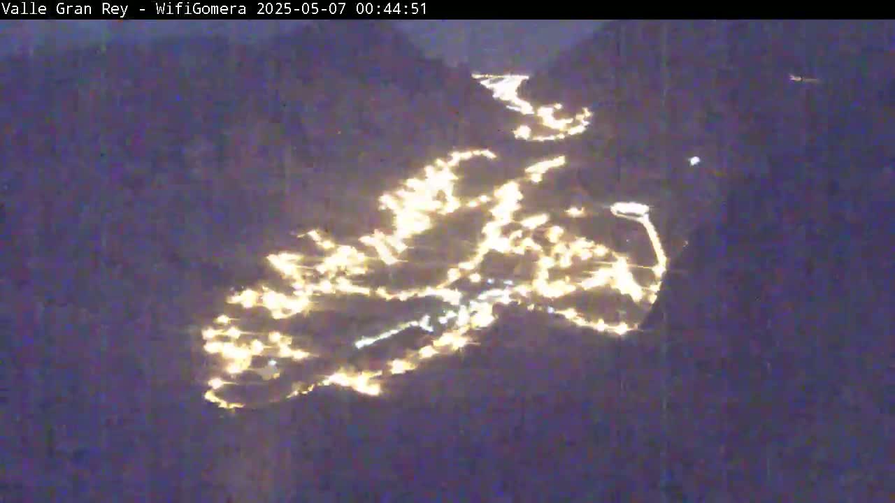 A nighttime, long-range view shows a valley illuminated by numerous scattered lights.