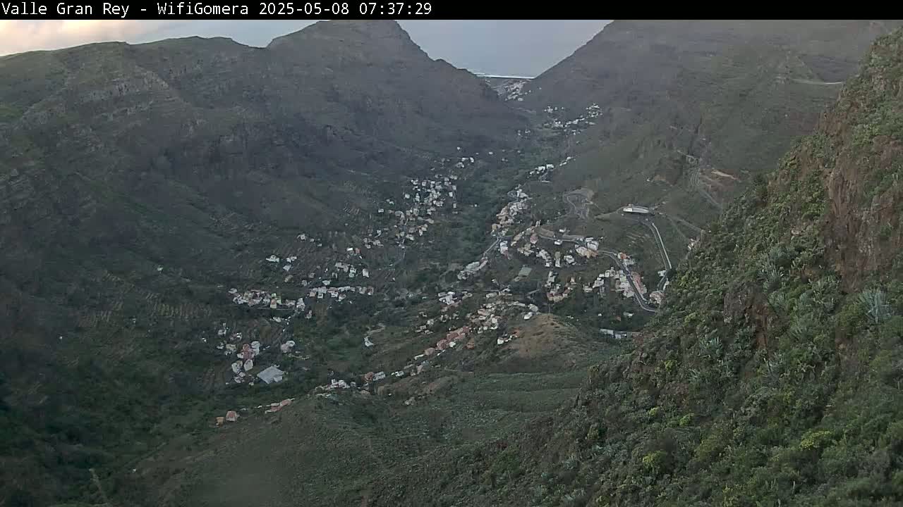 A mountain valley town nestled between steep, dark green hillsides under an overcast sky.