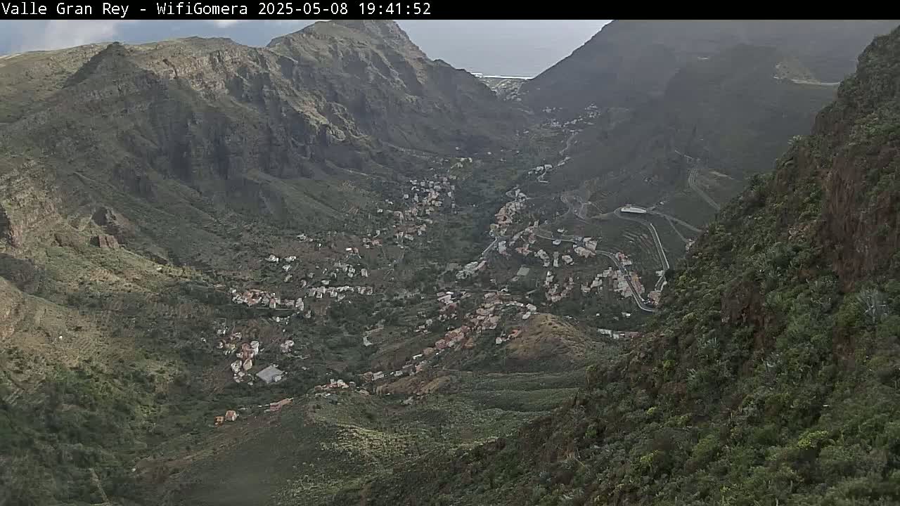 A mountain valley town nestled between steep, verdant hillsides under an overcast sky.