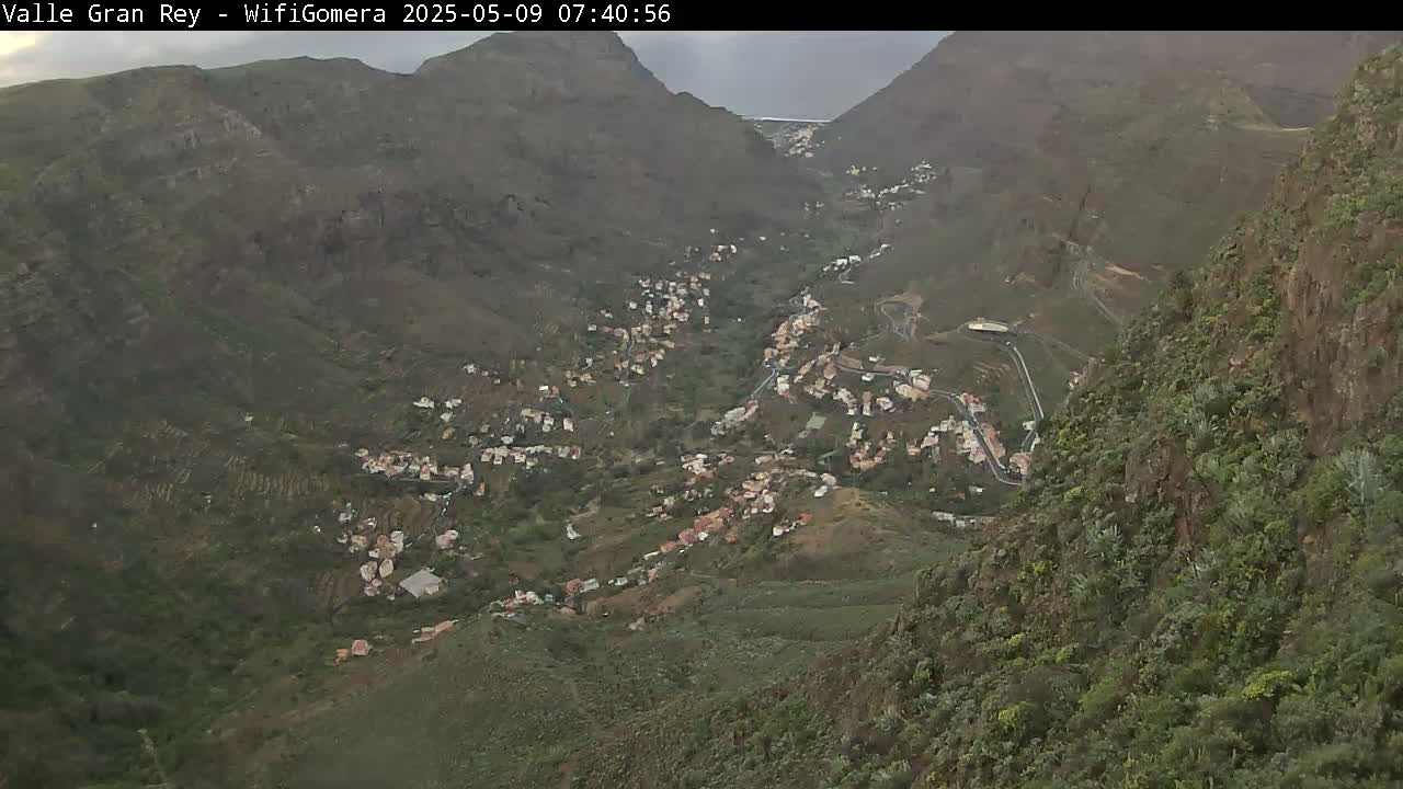 An overcast view from a mountaintop shows a valley town nestled among verdant hillsides and winding roads.