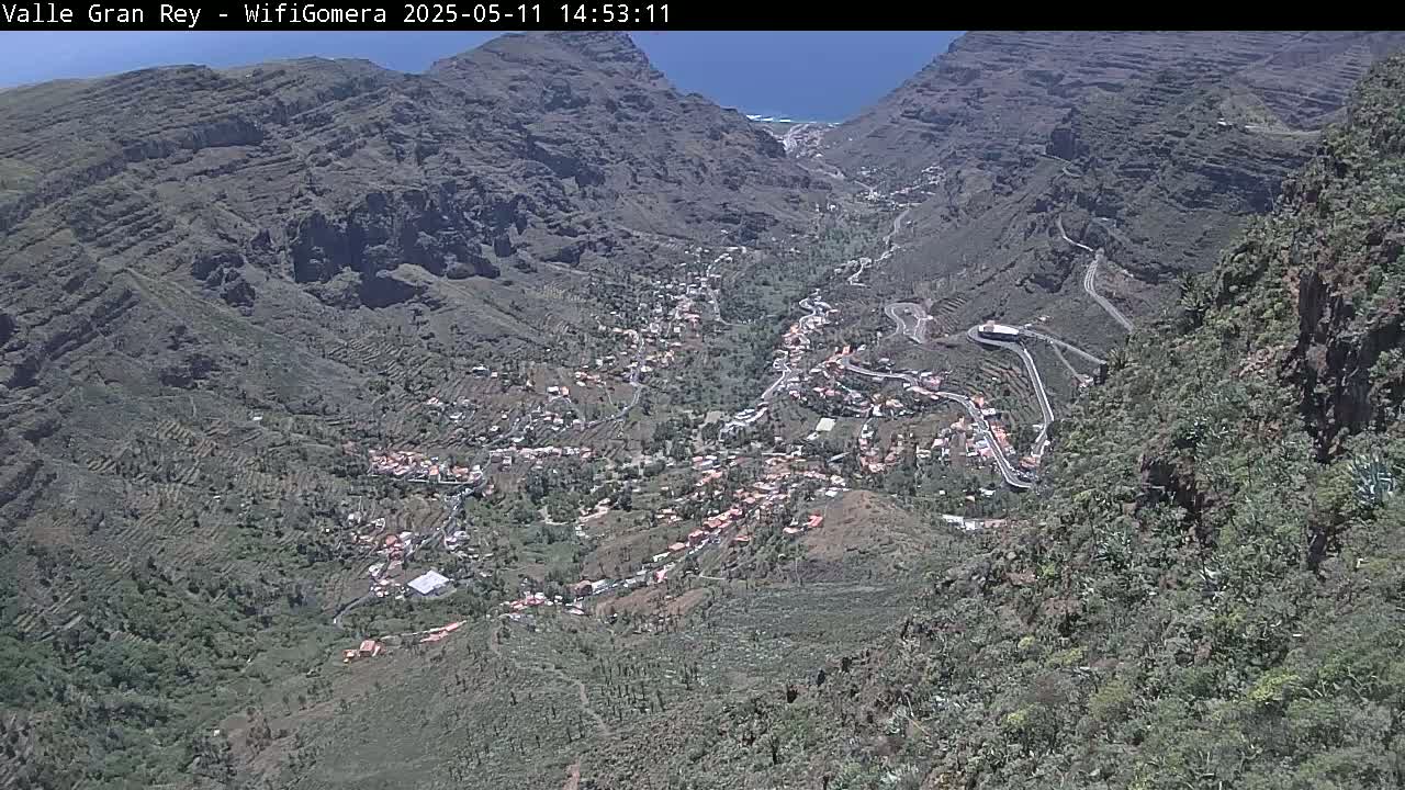 A mountain valley town nestled between steep, rocky cliffs under a bright, sunny sky.