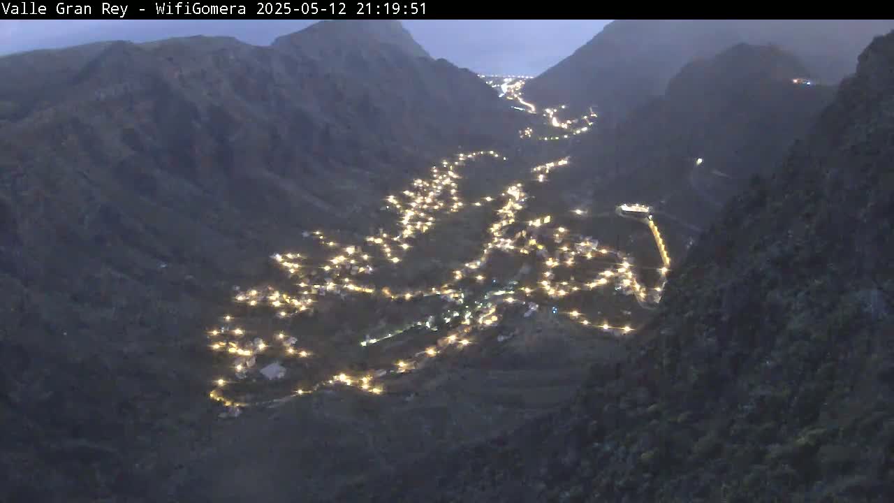 A valley nestled between dark mountains at night is illuminated by numerous small lights scattered across the landscape.