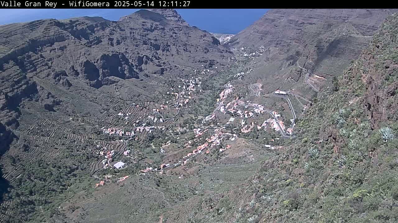 A village nestled in a steep, rocky valley under a clear blue sky.