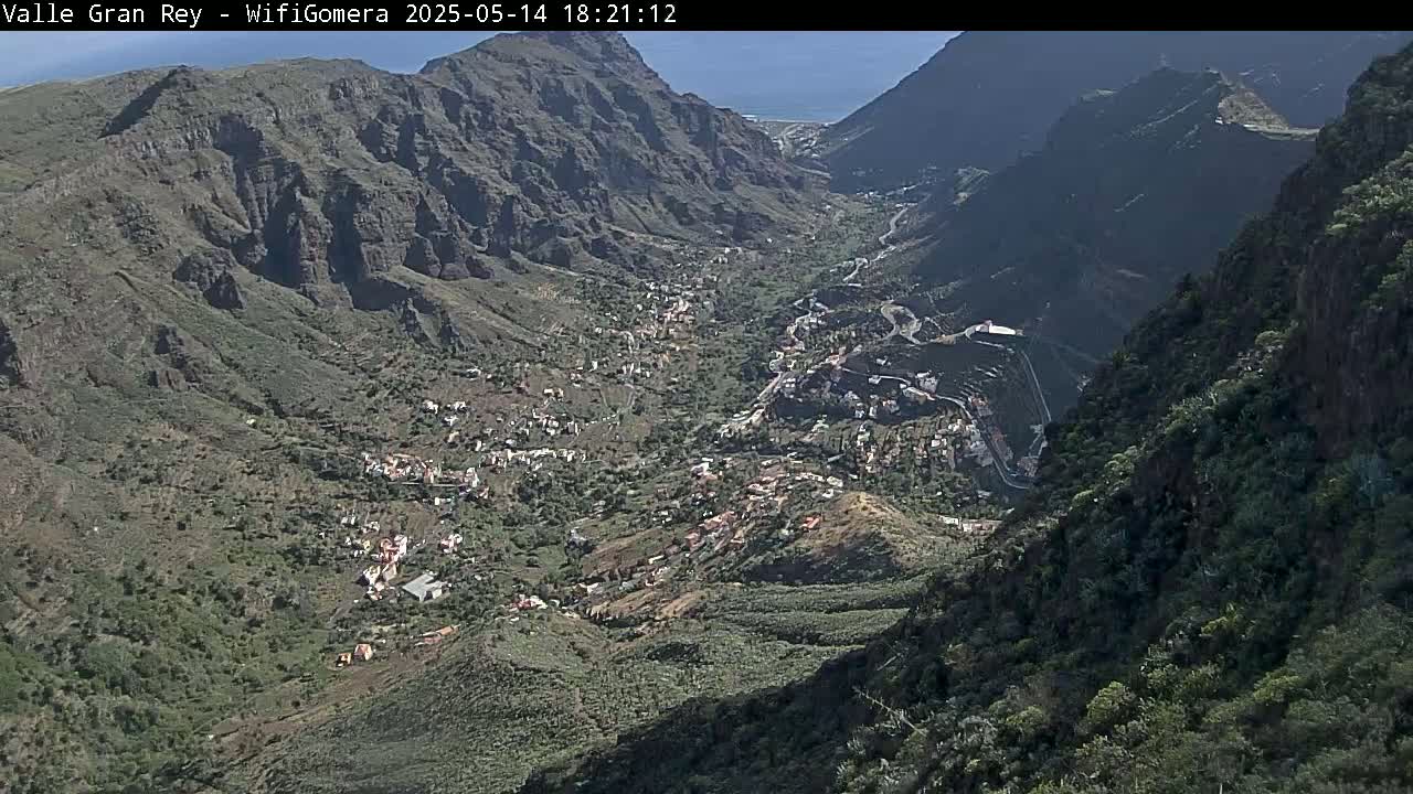 A sunny view from a mountaintop overlooking a valley town nestled between steep, rocky hillsides.