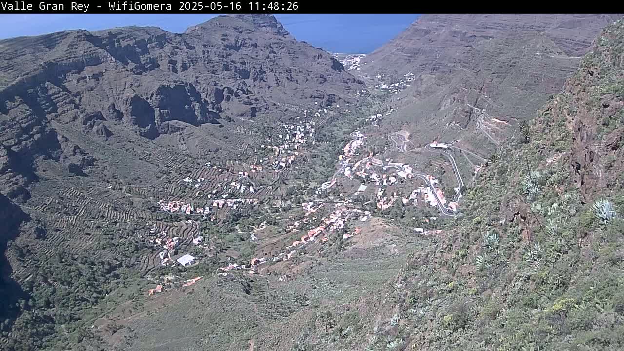A high-angle view shows a village nestled in a steep, rocky valley on a sunny day.