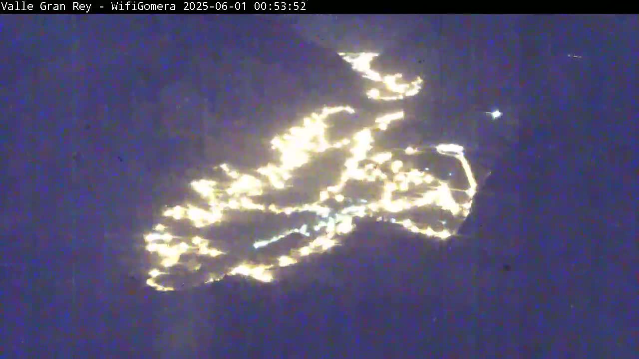 A nighttime aerial view shows a scattering of bright lights across a dark, possibly mountainous, landscape.