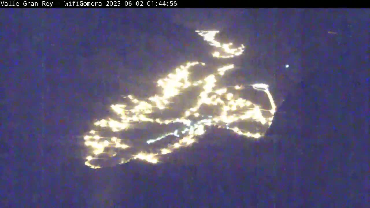 A nighttime long-range view shows a scattering of bright lights across a dark, possibly water, surface.