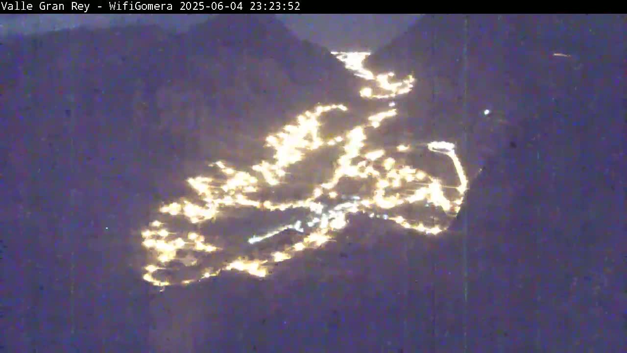 A nighttime aerial view shows a town nestled in a valley between dark mountains.