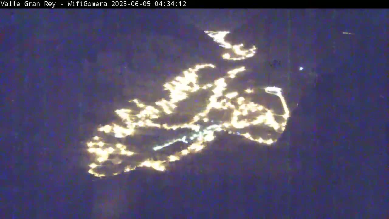 A nighttime aerial view shows city lights reflecting on a dark body of water.