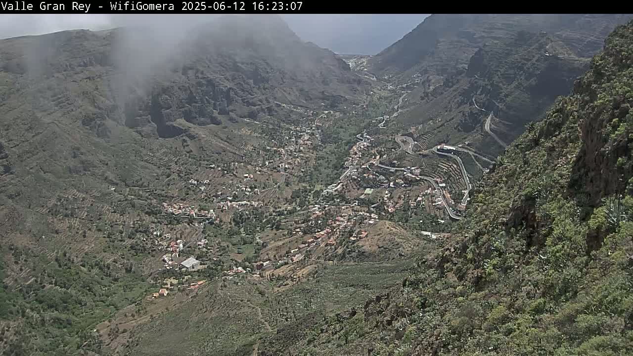 A hazy view overlooks a mountainous valley town with winding roads and terraced farmland.