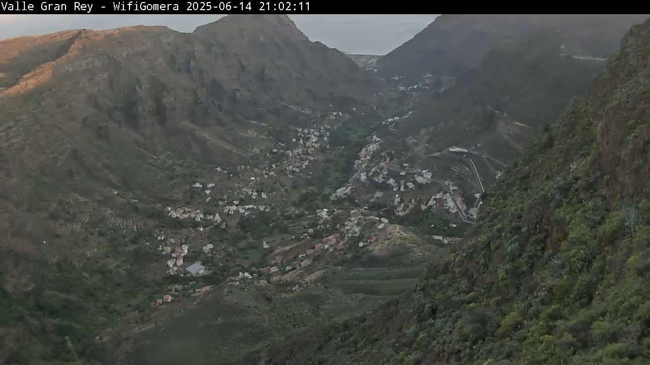 A mountainous valley town is nestled between steep, rocky cliffs under a mostly clear sky.