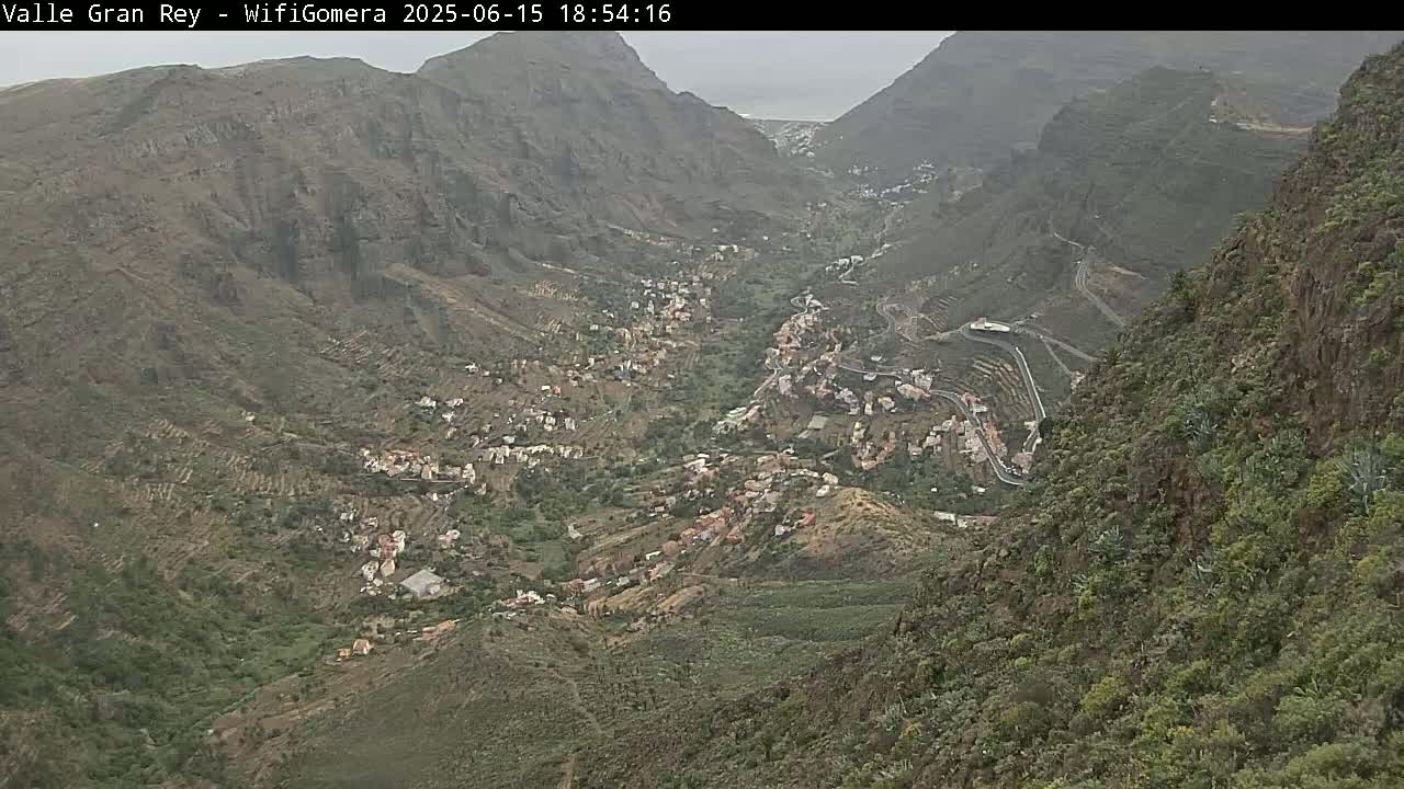 A hillside village nestled in a steep, rocky valley under an overcast sky.