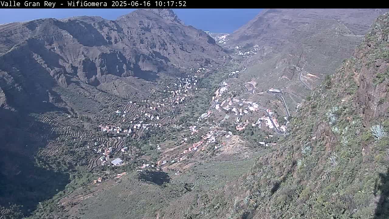 A mountain valley town nestled among terraced hillsides under a clear blue sky.