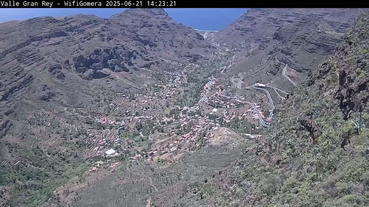 A mountain village nestled in a valley between steep, rocky mountains on a sunny day.