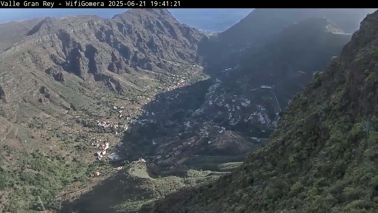 A high-angle view shows a sunlit valley nestled between steep, dark mountains, with a small town visible in the valley.