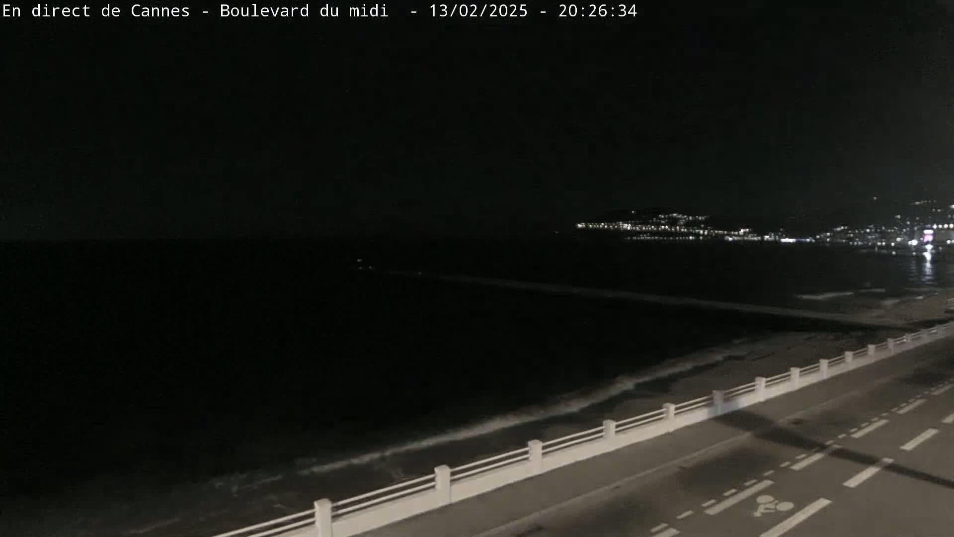 A nighttime view of a dark ocean with gentle waves lapping against a seawall next to a roadway.