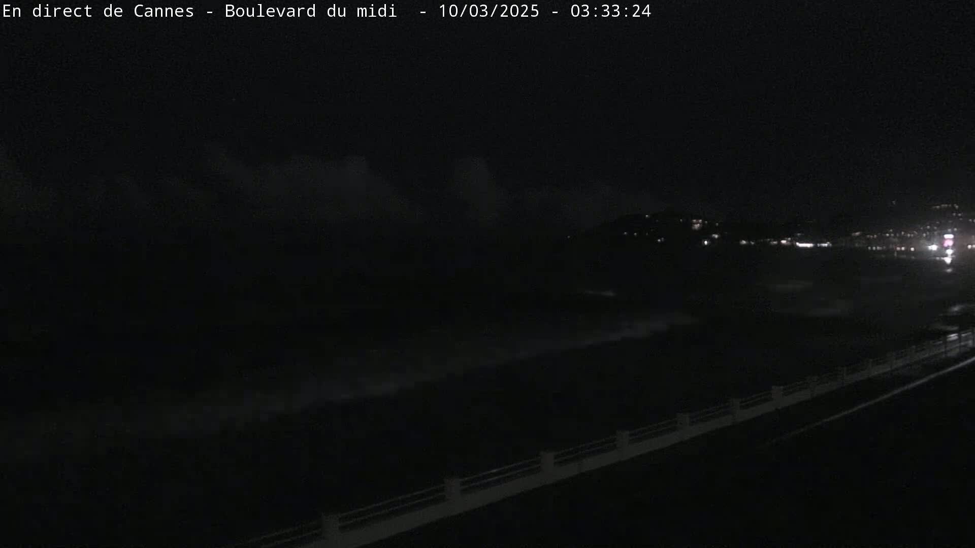 A nighttime view of a dark ocean with waves crashing against a shoreline, under a cloudy sky.