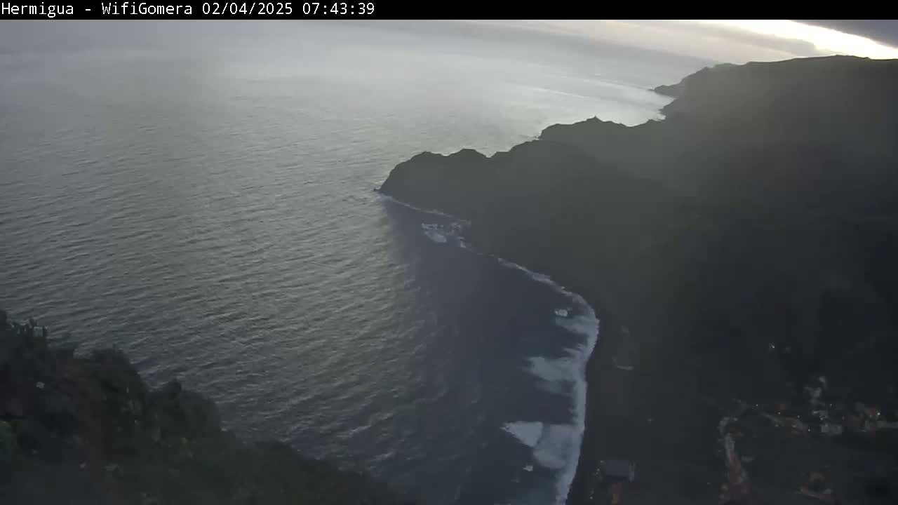 A high-angle view shows a dark, rocky coastline meeting a dark ocean under an overcast sky.
