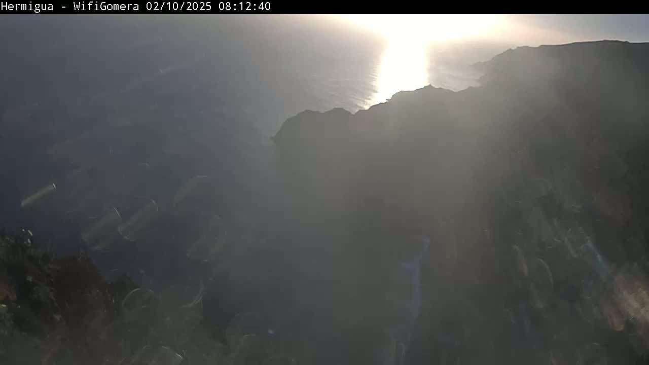 A hazy sunrise illuminates a dark, rocky coastline and the ocean below.