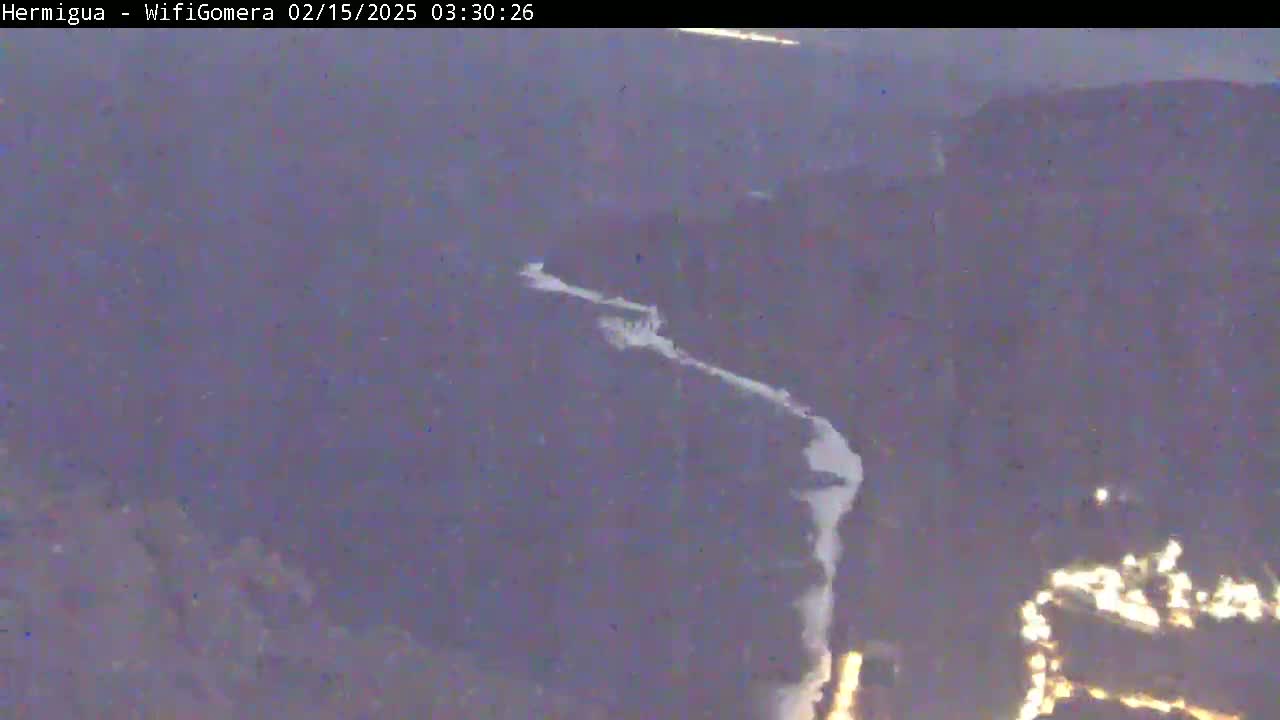 A high-angle, long shot shows a winding, light-colored river or stream snaking through a dark, mountainous landscape at night.
