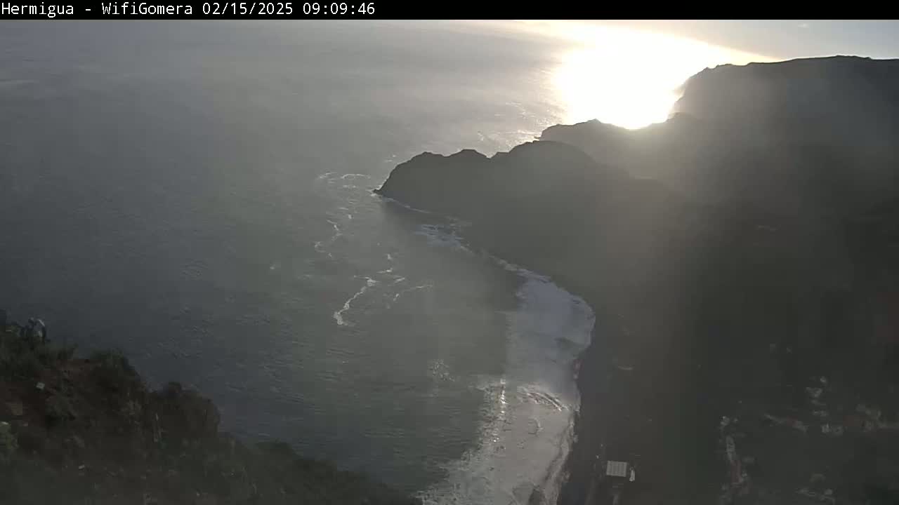 A hazy sunrise illuminates a rocky coastline where dark cliffs meet a somewhat turbulent ocean.