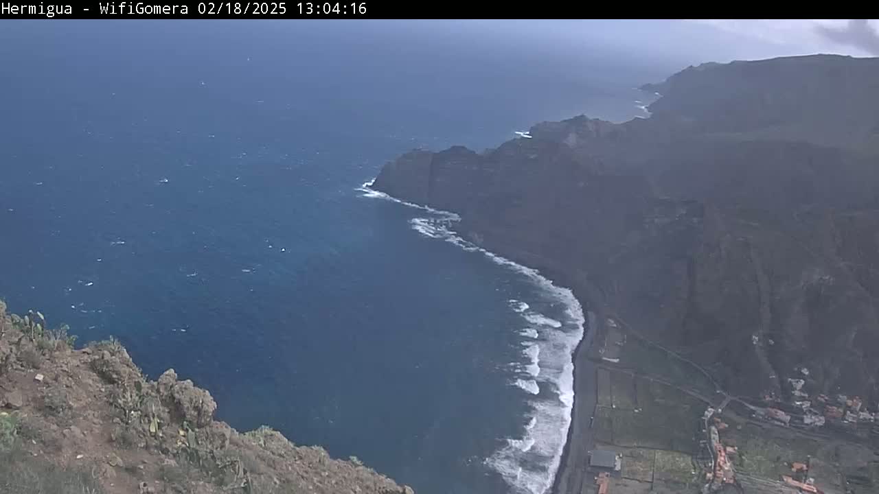 A high-angle view shows dark-colored cliffs meeting a dark blue ocean with white-capped waves under an overcast sky.