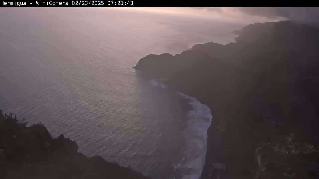 A high-angle view shows dark cliffs meeting a calm, dusky ocean under a hazy sky at dawn or dusk.
