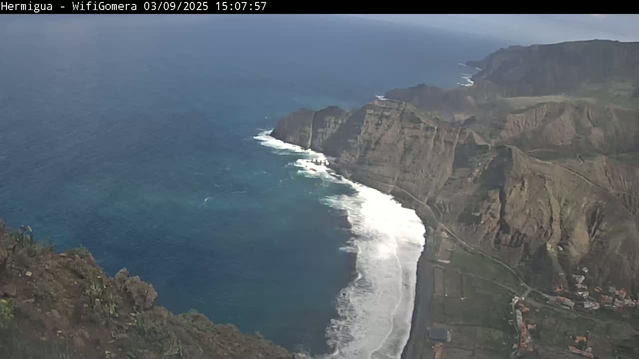 High-angle view of a rocky coastline with crashing waves on a partly sunny day.