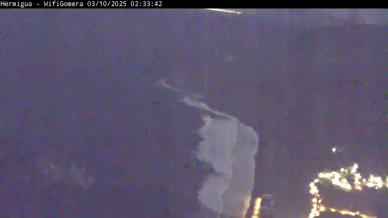 A nighttime, blurry aerial view shows a dark landscape with a lighter, possibly cloudy or snowy, area in the center.