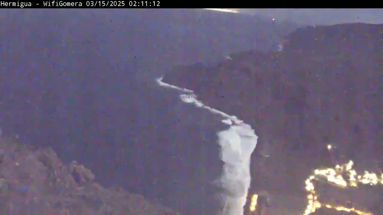 A long, white waterfall cascades down a dark, rocky cliff at night.