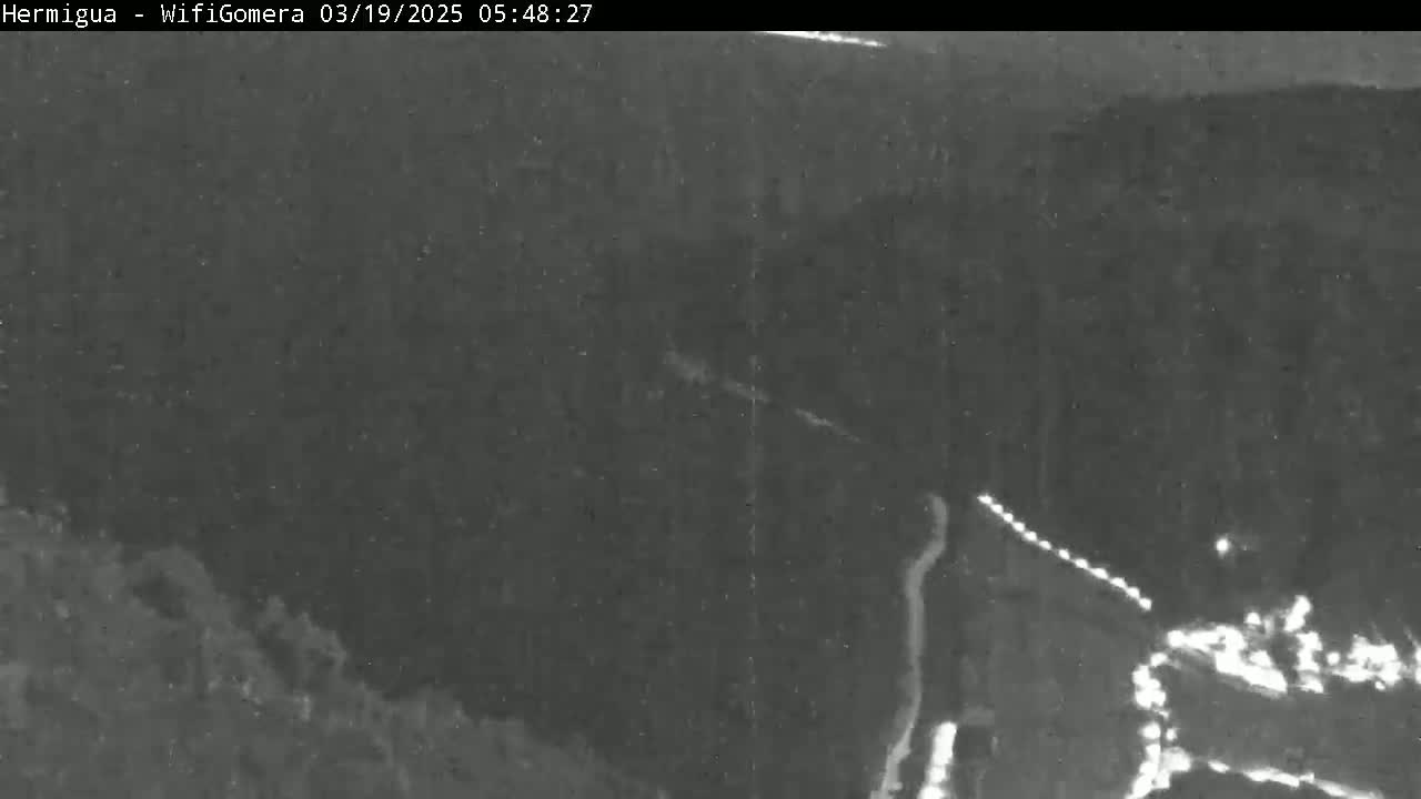 A nighttime, low-light image shows a winding road curving through a dark, hilly landscape.