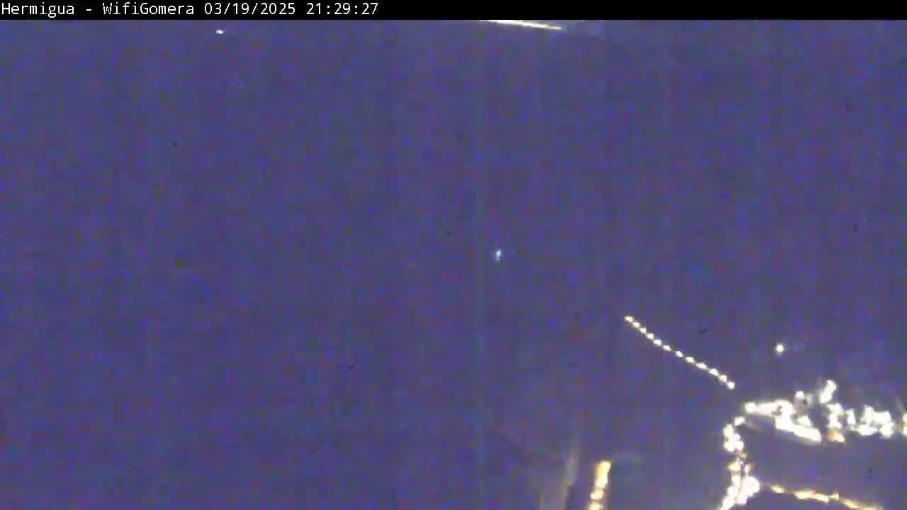 A nighttime, dark purple sky shows a string of lights possibly from a satellite or airplane, and a brighter cluster of lights in the lower right corner.