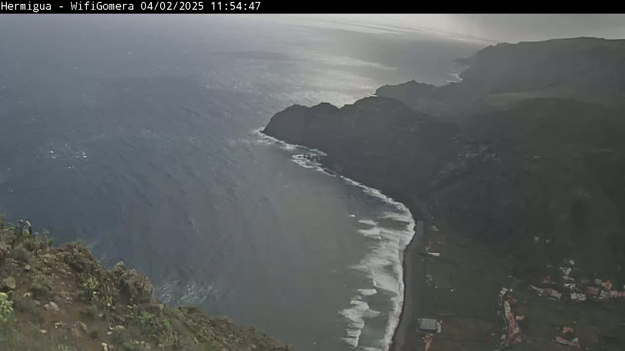 A high-angle view shows a rocky, dark coastline meeting a choppy, gray sea under an overcast sky.