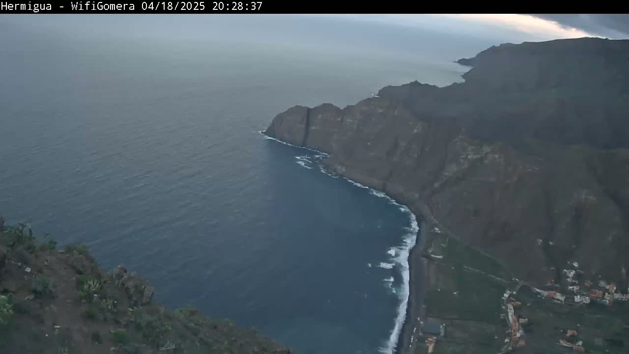 A high-angle, long shot shows dark cliffs meeting a dark-blue ocean under a cloudy sky.