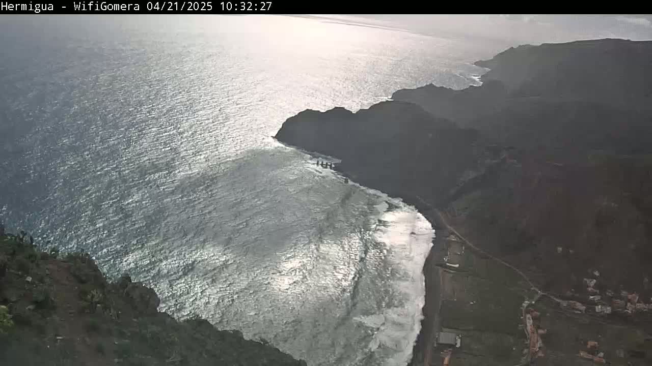 An aerial view shows a rocky coastline with crashing waves on a partly sunny day.