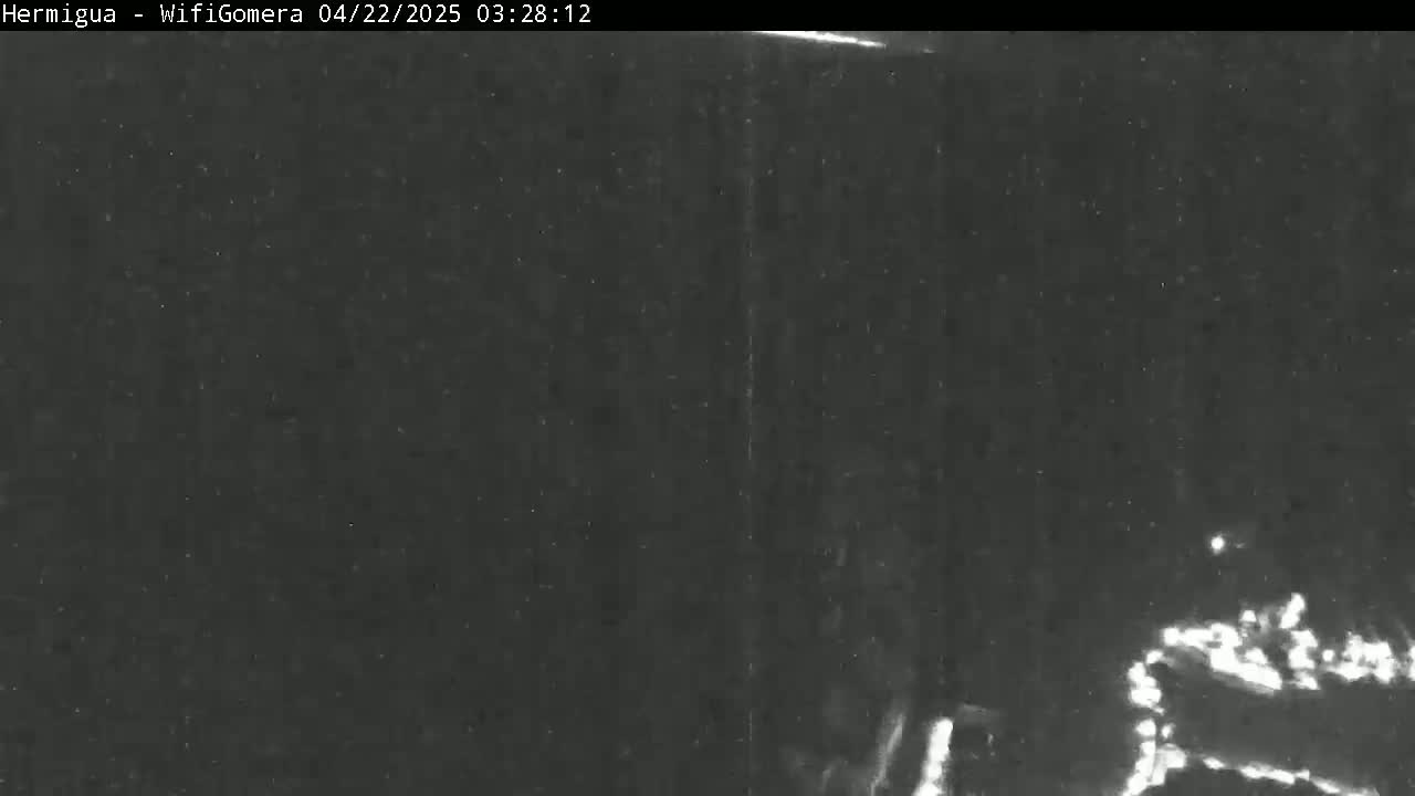 A low-light nighttime image shows a dark, possibly overcast scene with faint, indistinct lights visible in the lower-right corner.