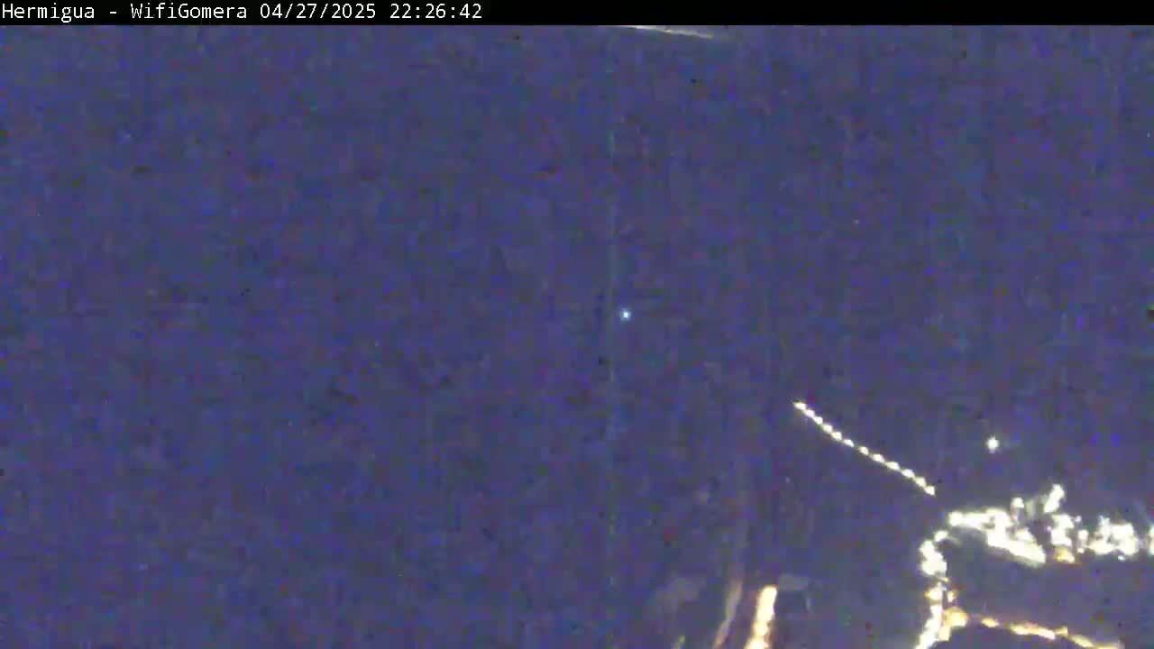 A nighttime, low-light image shows a blurry view of the night sky with a bright light and a long streak of lights, possibly from a satellite or aircraft.