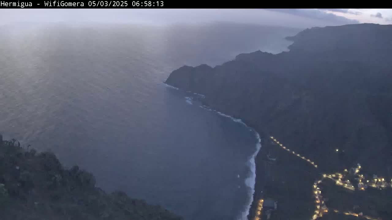 A hazy, dusky view shows a dark, mountainous coastline meeting a dark ocean with small waves.
