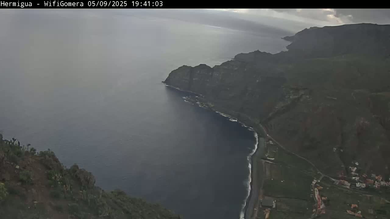 A high-angle view shows a dark, overcast day over a rugged coastline where dark cliffs meet a dark-blue ocean.
