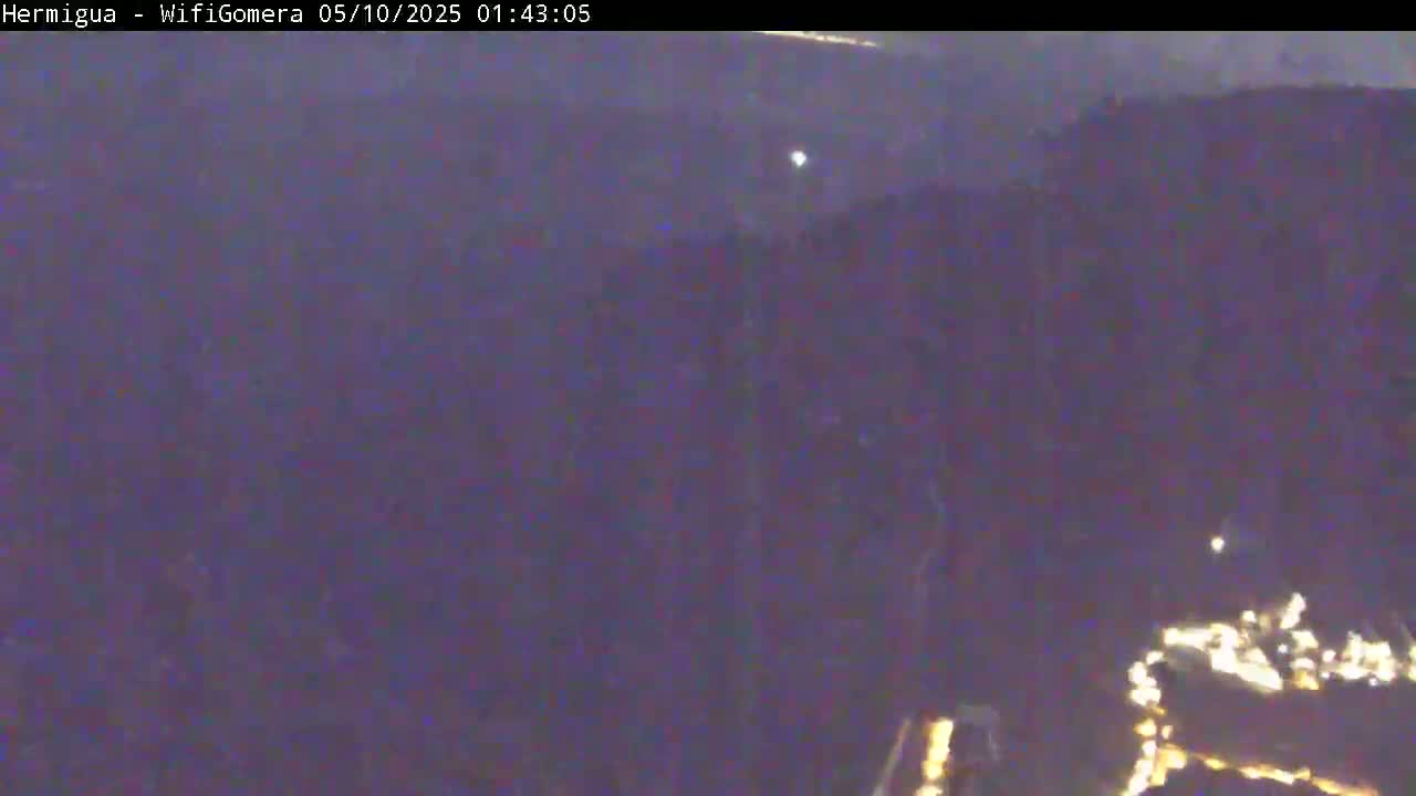 A dark, nighttime view shows a blurry landscape with a few distant lights and a hazy atmosphere.