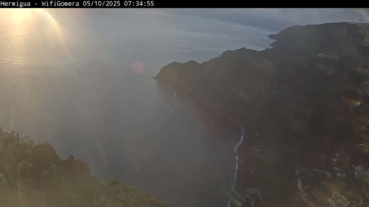 A hazy sunrise illuminates a coastal cliffside overlooking a calm ocean.