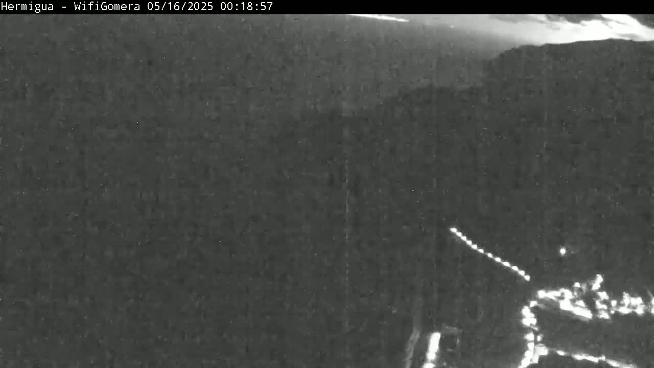 A nighttime, low-light image shows a dark landscape with a faintly visible road and lights in the bottom right corner, possibly indicating a vehicle or settlement.